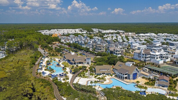 A resort with a large pool, multiple buildings, and a surrounding forest.