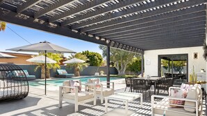 A covered outdoor area with a pool, lounge chairs, and a dining table.