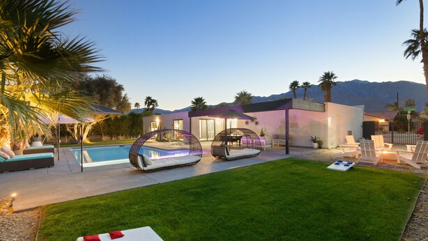 A modern outdoor pool area with lounge chairs, a grassy lawn, and a building with a unique architectural design.