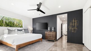 A modern bedroom with a bed, a ceiling fan, a TV, and a decorative wall piece.