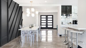 A modern kitchen with a dining area, featuring a white countertop, clear chairs, and a unique light fixture.