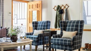 A room with two plaid armchairs, a small table with a book and a vase, and a coat rack with jackets. - Hartwood by Avantstay Cozy Big Bear Abode w/ Spacious Deck & Stone Fireplace (Big Bear Lake)