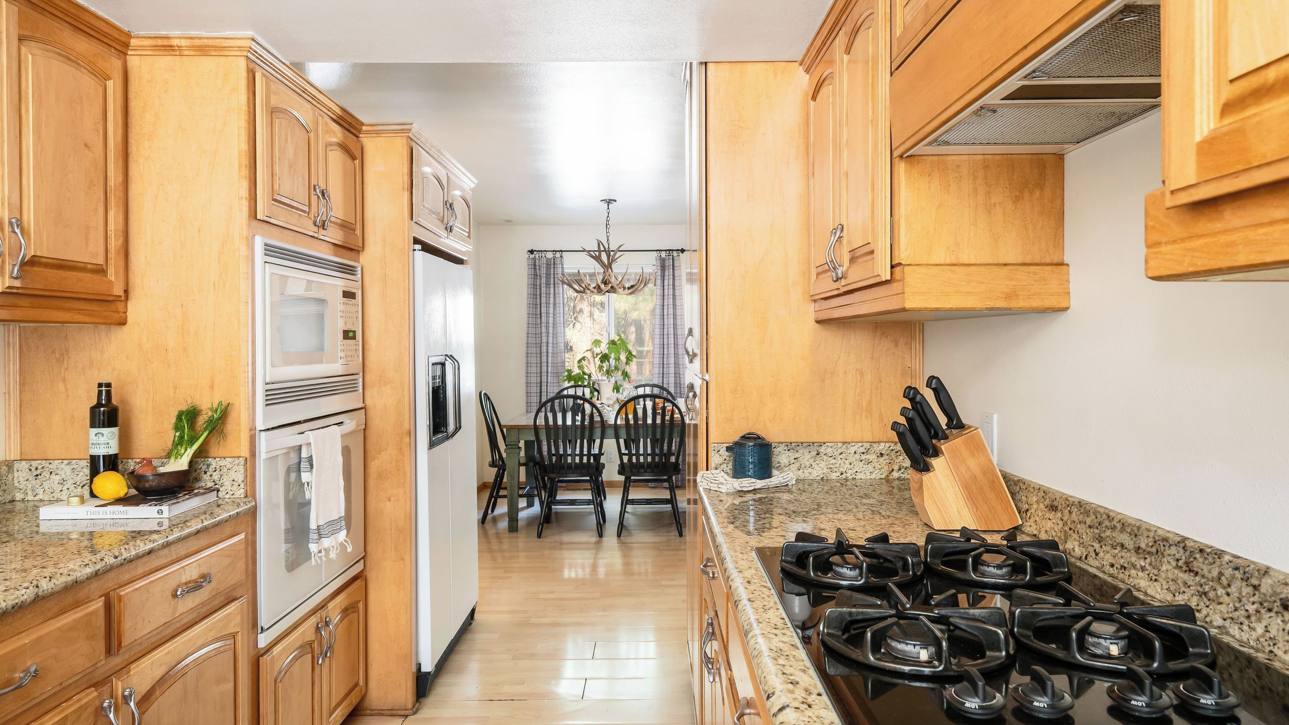 A kitchen with wooden cabinets, a gas stove, a refrigerator, and a dining area with chairs and a table.