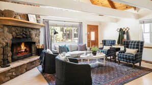 A cozy living room with a stone fireplace, comfortable seating, and a large window. - Hartwood by Avantstay Cozy Big Bear Abode w/ Spacious Deck & Stone Fireplace (Big Bear Lake)