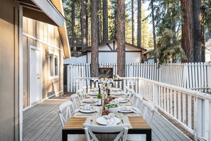 Ein Essbereich im Freien mit einer Holzterrasse, weißen Stühlen und einem für eine Mahlzeit gedecktem Tisch.
