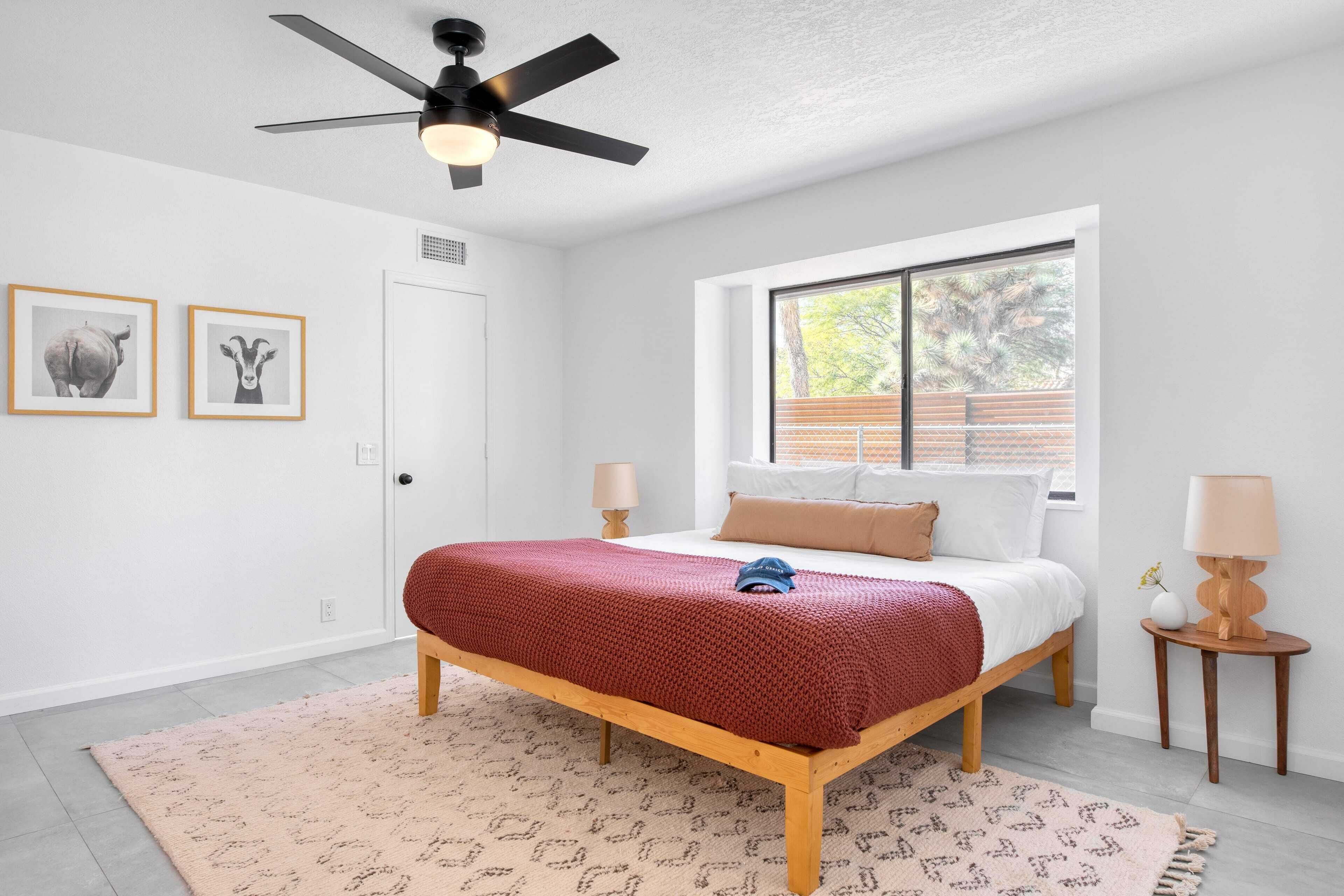 A bedroom with a bed, a ceiling fan, a window, and two wall-mounted lamps.