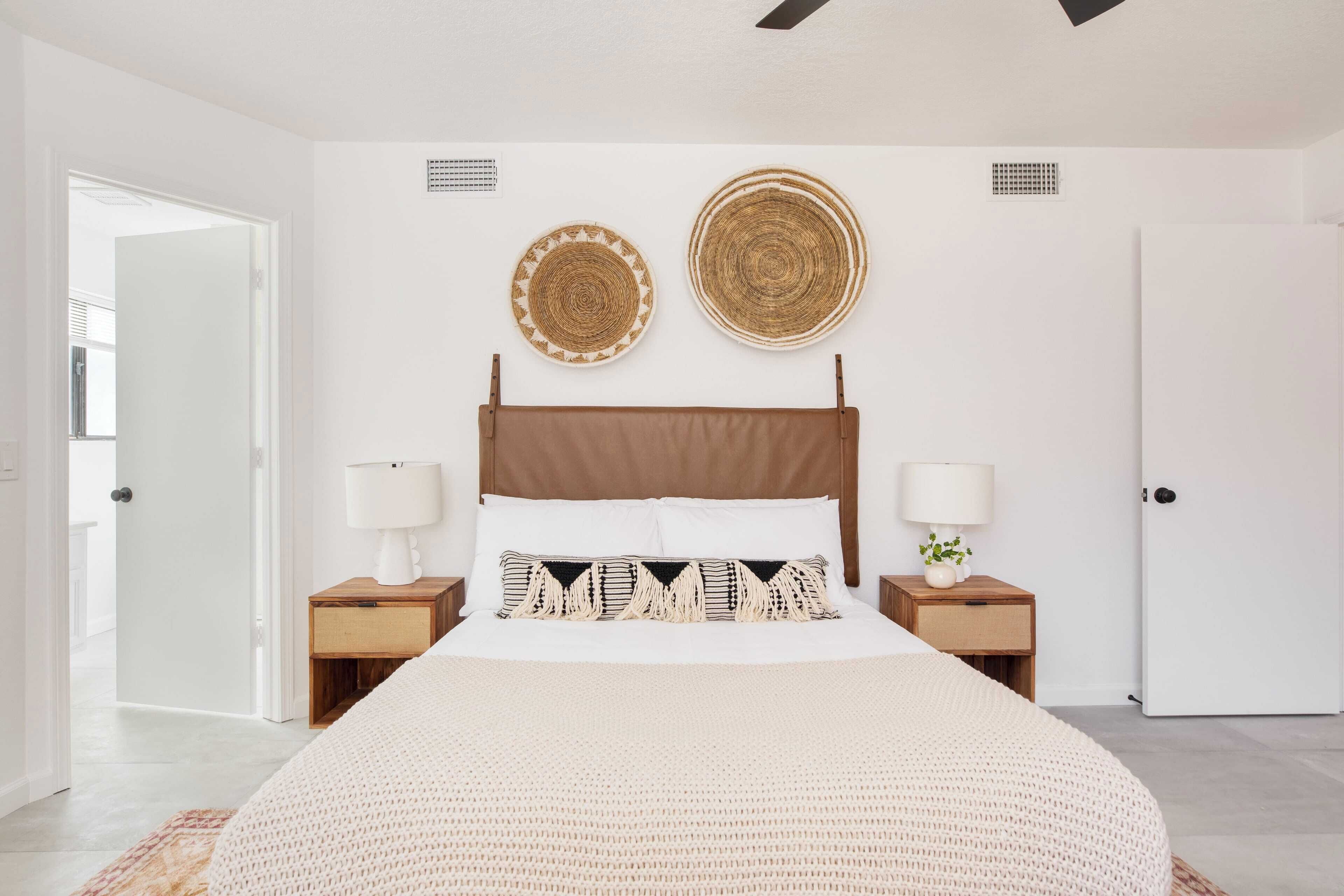 A bedroom with a large bed, two bedside tables with lamps, and two wall-mounted woven baskets.