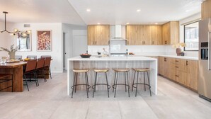 Eine moderne Küche mit Holzausstattung, einer zentralen Kochinsel mit Barhocker und einem Essbereich mit Holztisch und Stühlen.