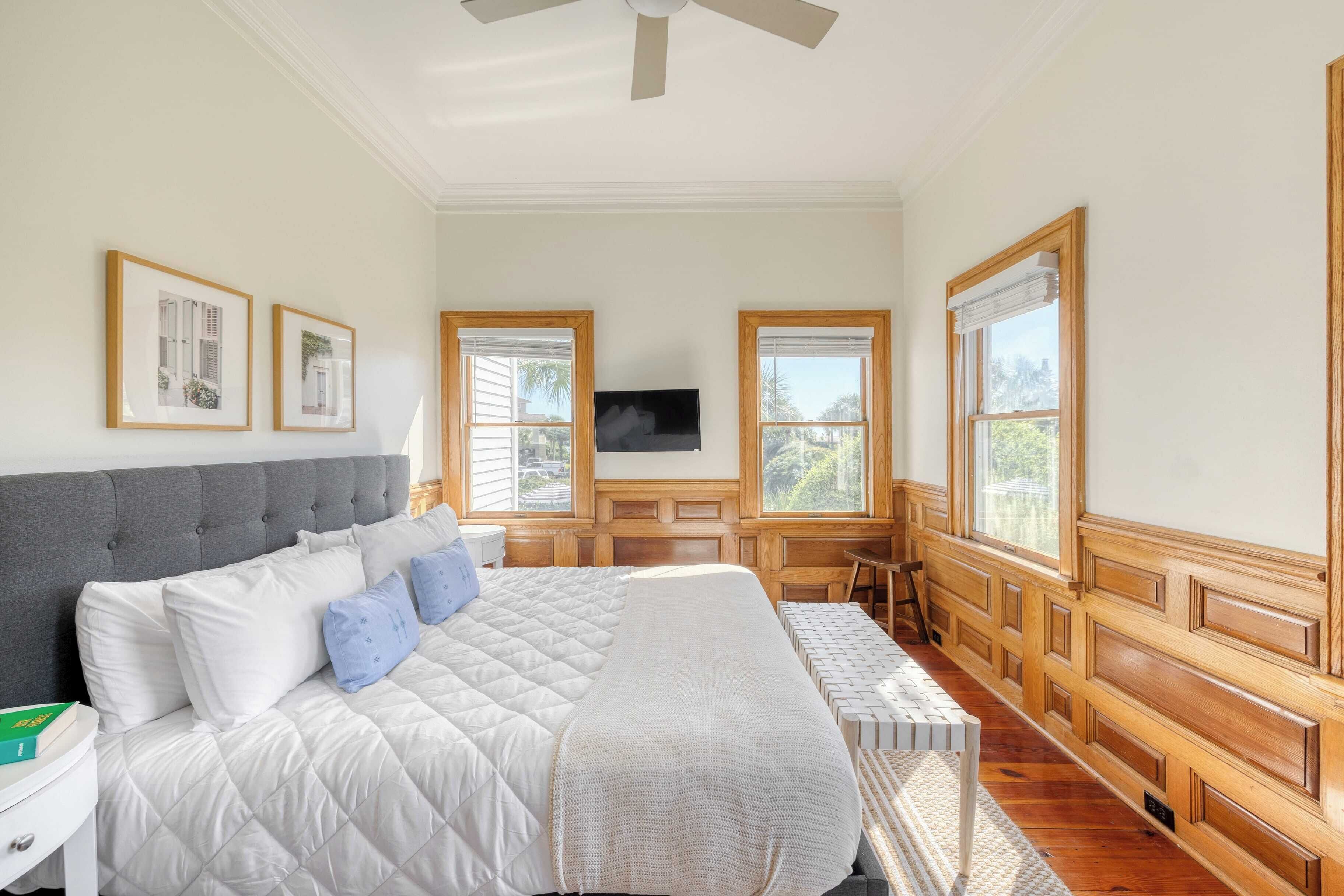 A bedroom with a large bed, a TV, wooden paneled walls, and multiple windows.