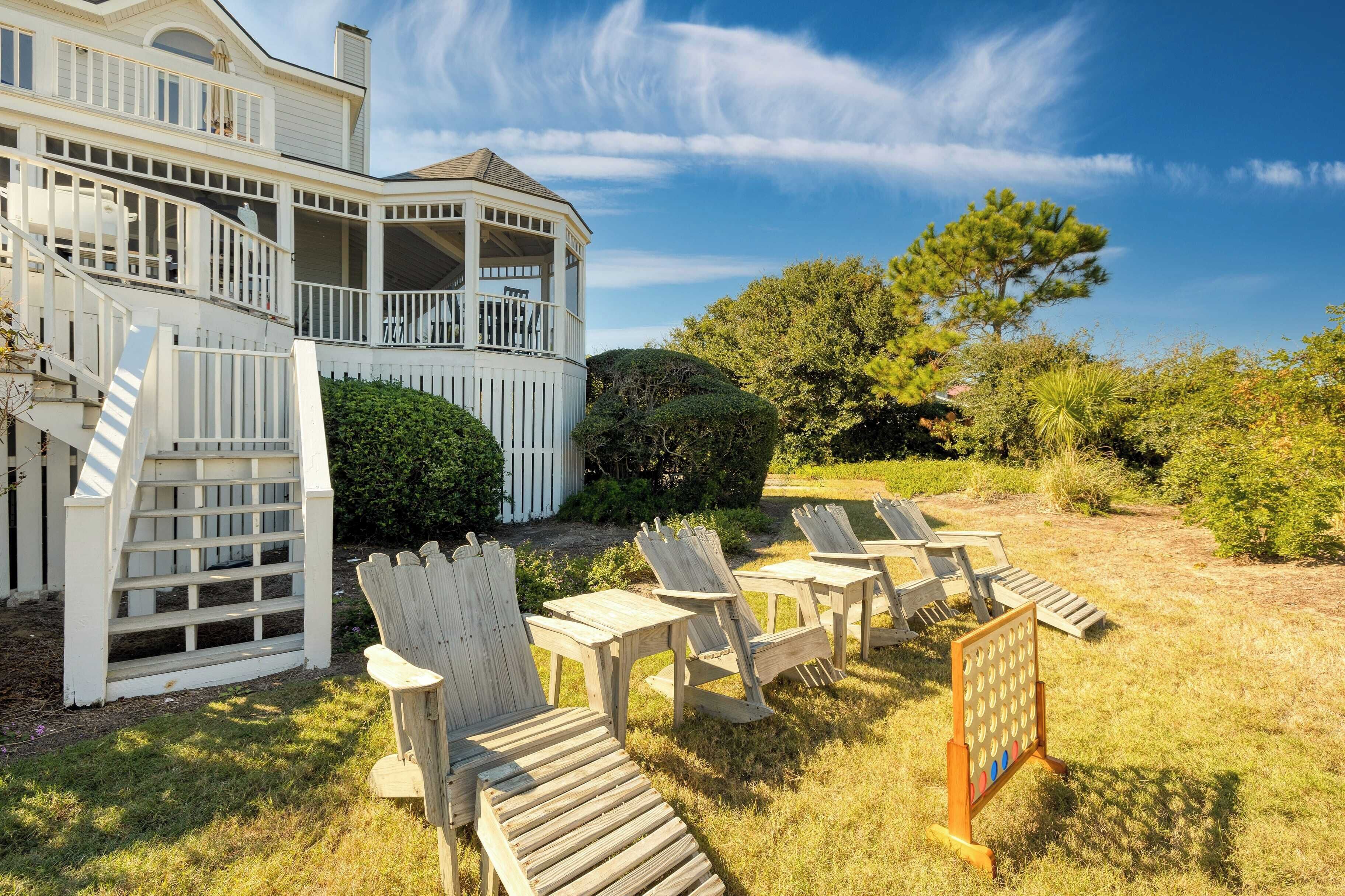 A large white house with a balcony, outdoor seating area with Adirondack chairs, and a board game.