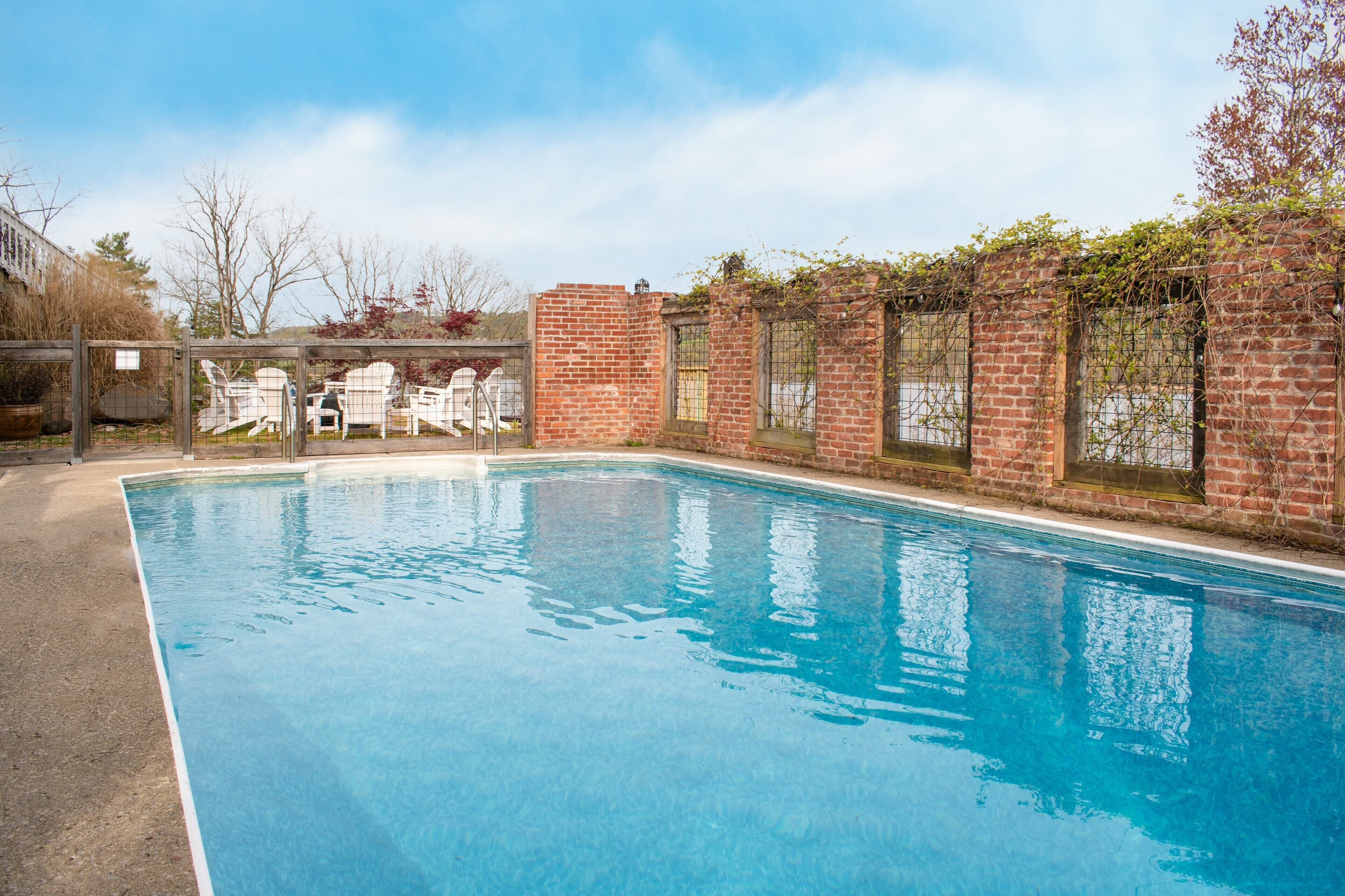 A rectangular swimming pool with clear blue water, surrounded by a brick wall with vines.