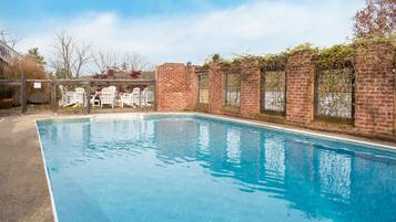 A rectangular swimming pool with clear blue water, surrounded by a brick wall with vines.