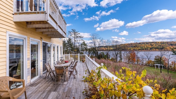 A wooden deck with a table and chairs, overlooking a lake and autumn foliage. - Shakespeare on the Hudson by Avantstay Two Home Buyout on the Hudson River! 22 Bedrooms! (Catskill)