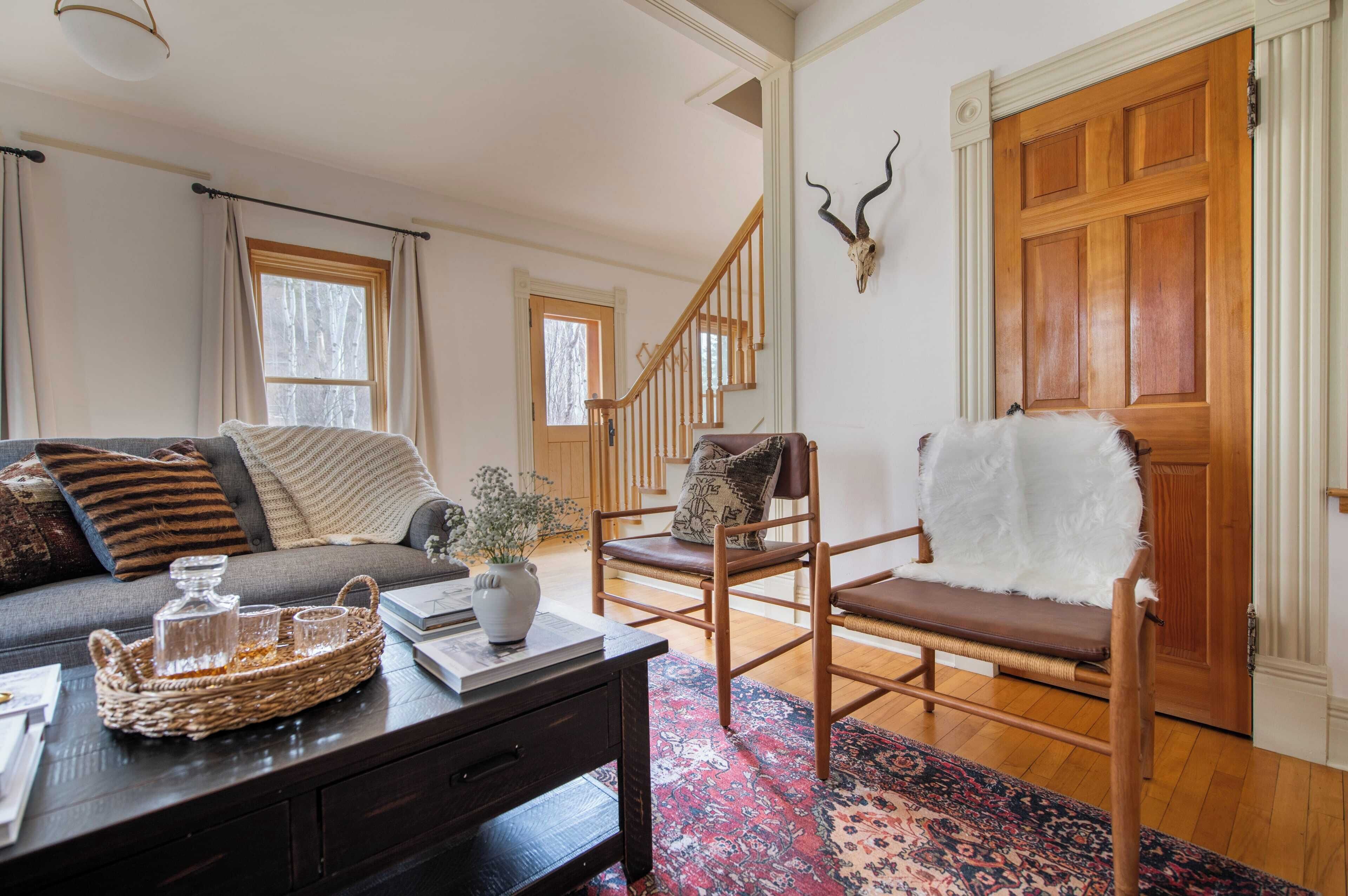 A cozy living room with a sofa, a chair, a wooden floor, a patterned rug, and a wooden staircase.