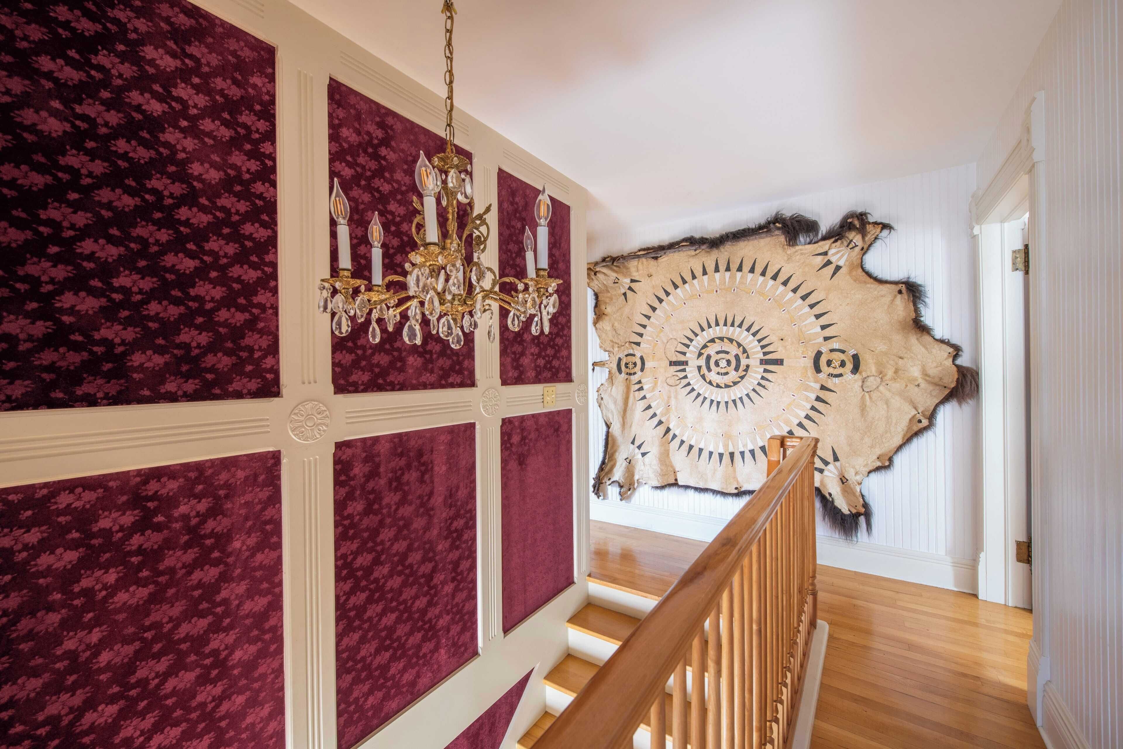 A staircase with a chandelier and a large Native American headdress on the wall.