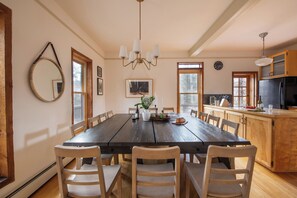 A dining area with a wooden table and chairs, a chandelier, and a kitchen with wooden cabinets and appliances.