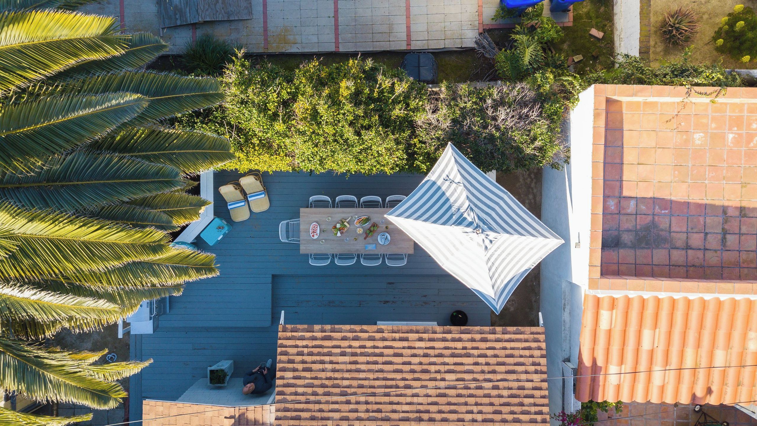 An outdoor dining area with a table and chairs, surrounded by greenery and a tiled roof.