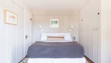 A bedroom with a bed, two bedside tables, a nightstand, a framed picture on the wall, and a door.