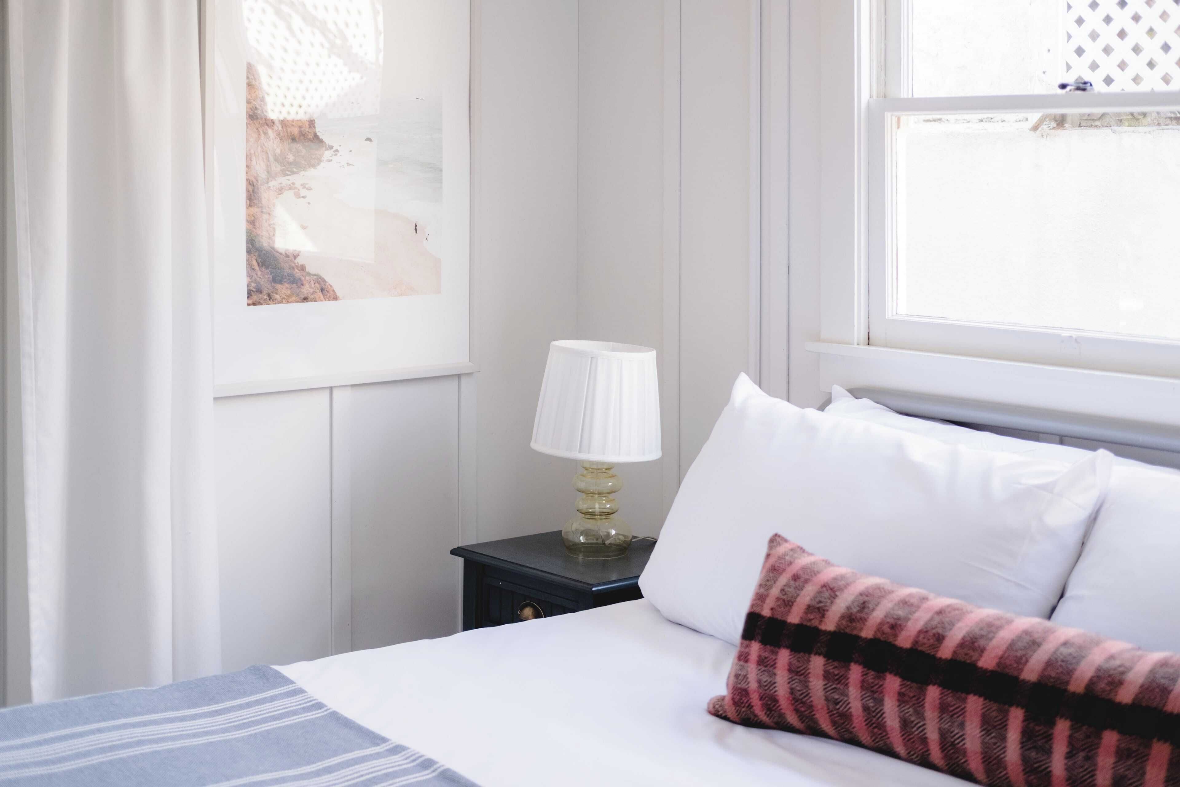 A neatly made bed with white and striped bedding, a lamp on a bedside table, and a framed picture on the wall.