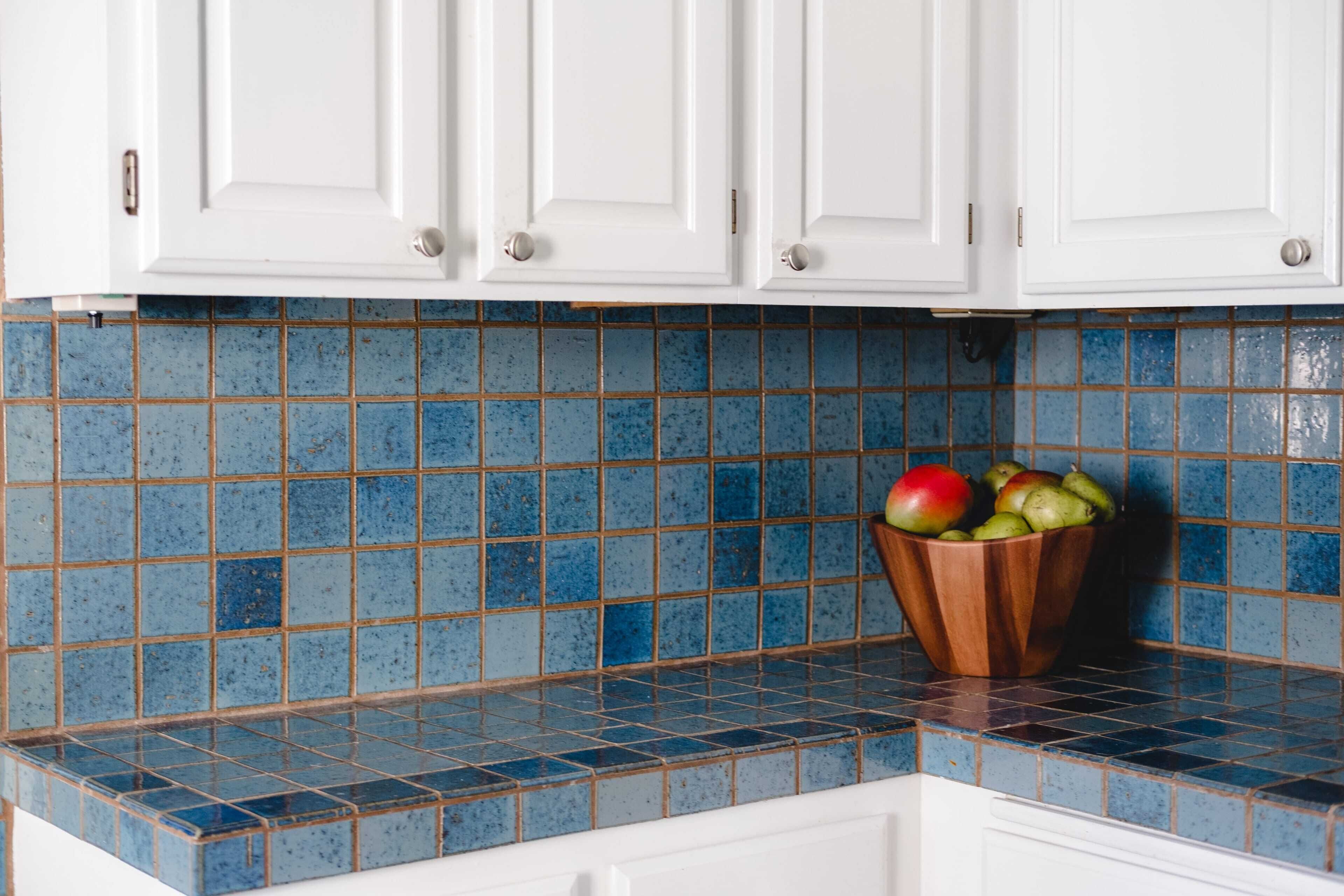 A kitchen with white cabinets and blue-tiled backsplash.