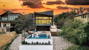 Ein modernes Haus mit Pool, überdachter Terrasse und Blick auf den Sonnenuntergang.