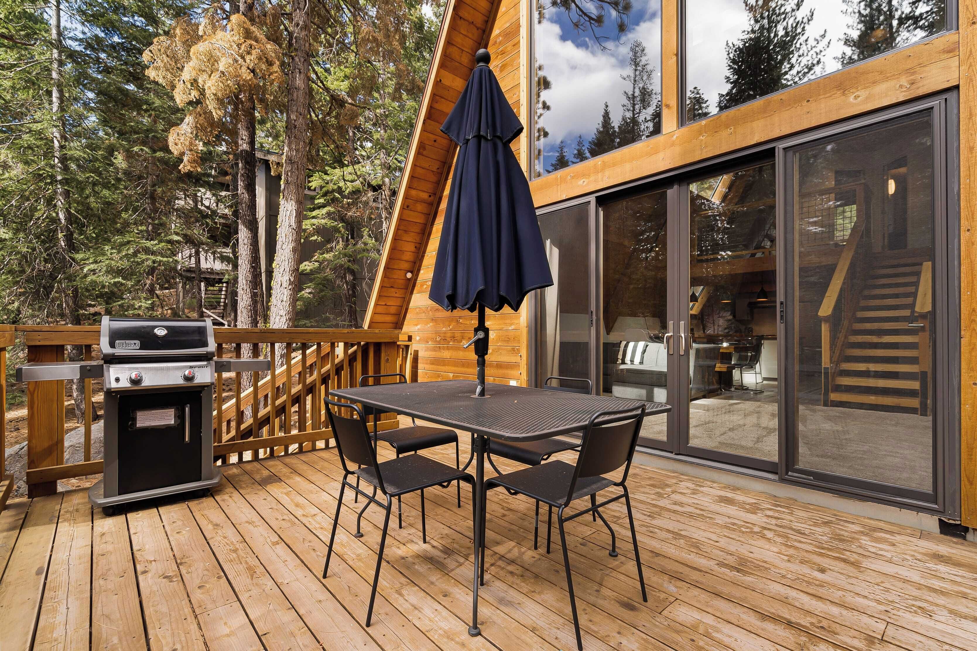 A wooden deck with a grill, a table with chairs, and an umbrella.