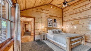 Un dormitori de cabana de fusta amb un llit, un ventilador de sostre i una finestra amb cortines.