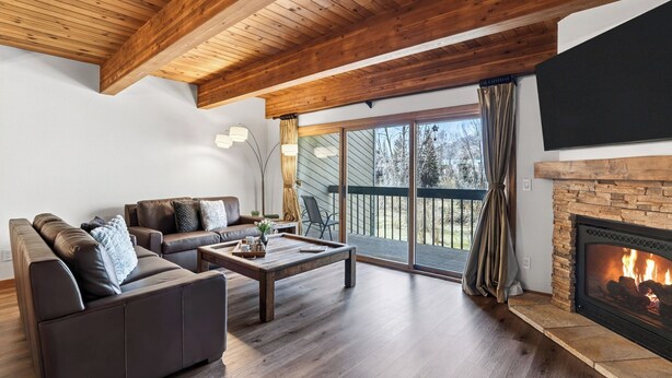 A living room with a fireplace, a sofa, a coffee table, and a sliding glass door leading to a balcony. - Riverside Condos C102 by Avantstay Condo Close To Downtown, Town Park & Ski Lift #8 (Telluride)