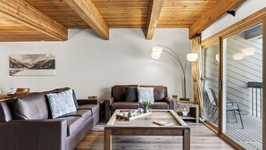 A cozy living room with wooden beams, leather sofas, a coffee table, and a large window with curtains. - Riverside Condos C102 by Avantstay Condo Close To Downtown, Town Park & Ski Lift #8 (Telluride)