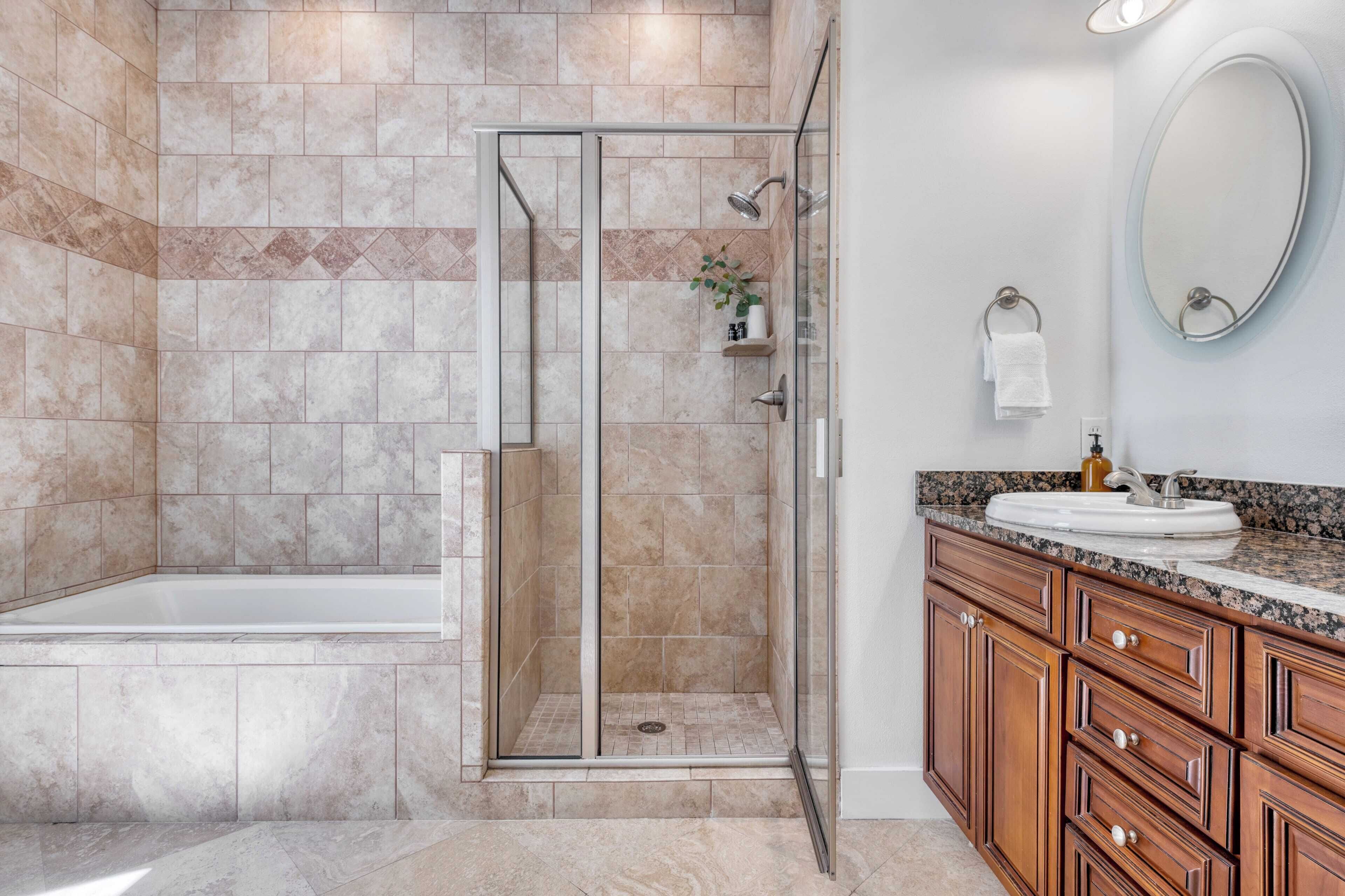 Ein Badezimmer mit einer gläsernen Duschkabine, einer Badewanne, Holzschränken, einer Granit-Arbeitsplatte und einem wandmontierten Spiegel.