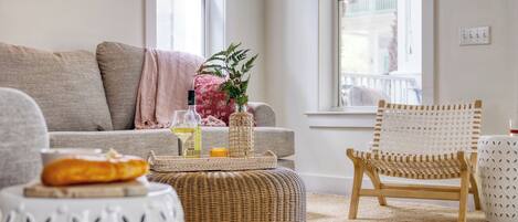 Un salón con sofá, reposapiés, sillón de mimbre y ventana con vistas.