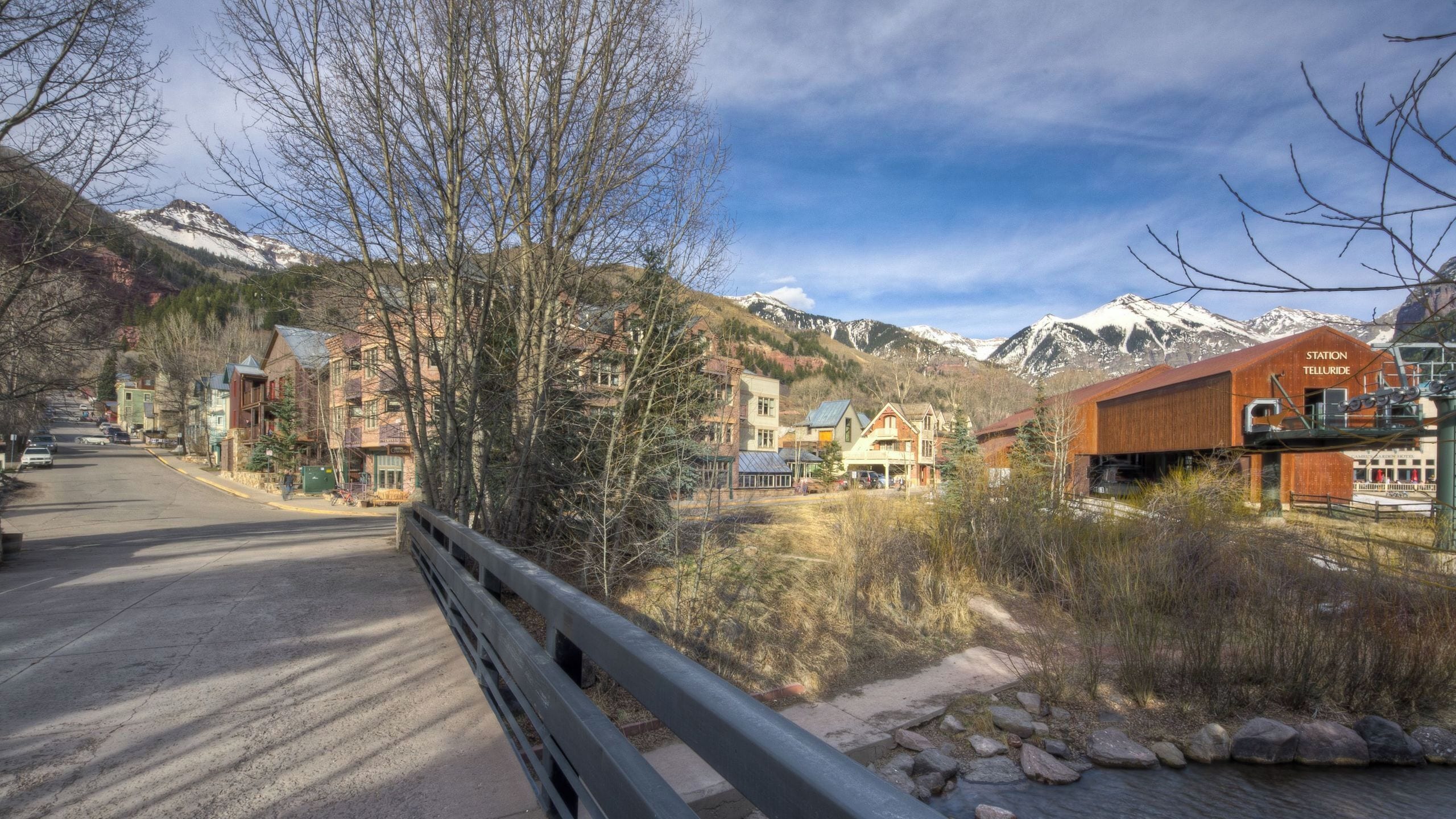 A mountain town with a mix of traditional and modern buildings, a railway station, and a road leading towards snow-capped mountains.