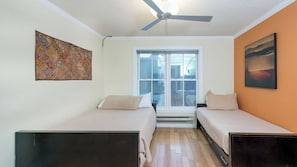 Una habitación pequeña con dos camas, un ventilador de techo, una ventana con vistas y un cuadro en la pared.