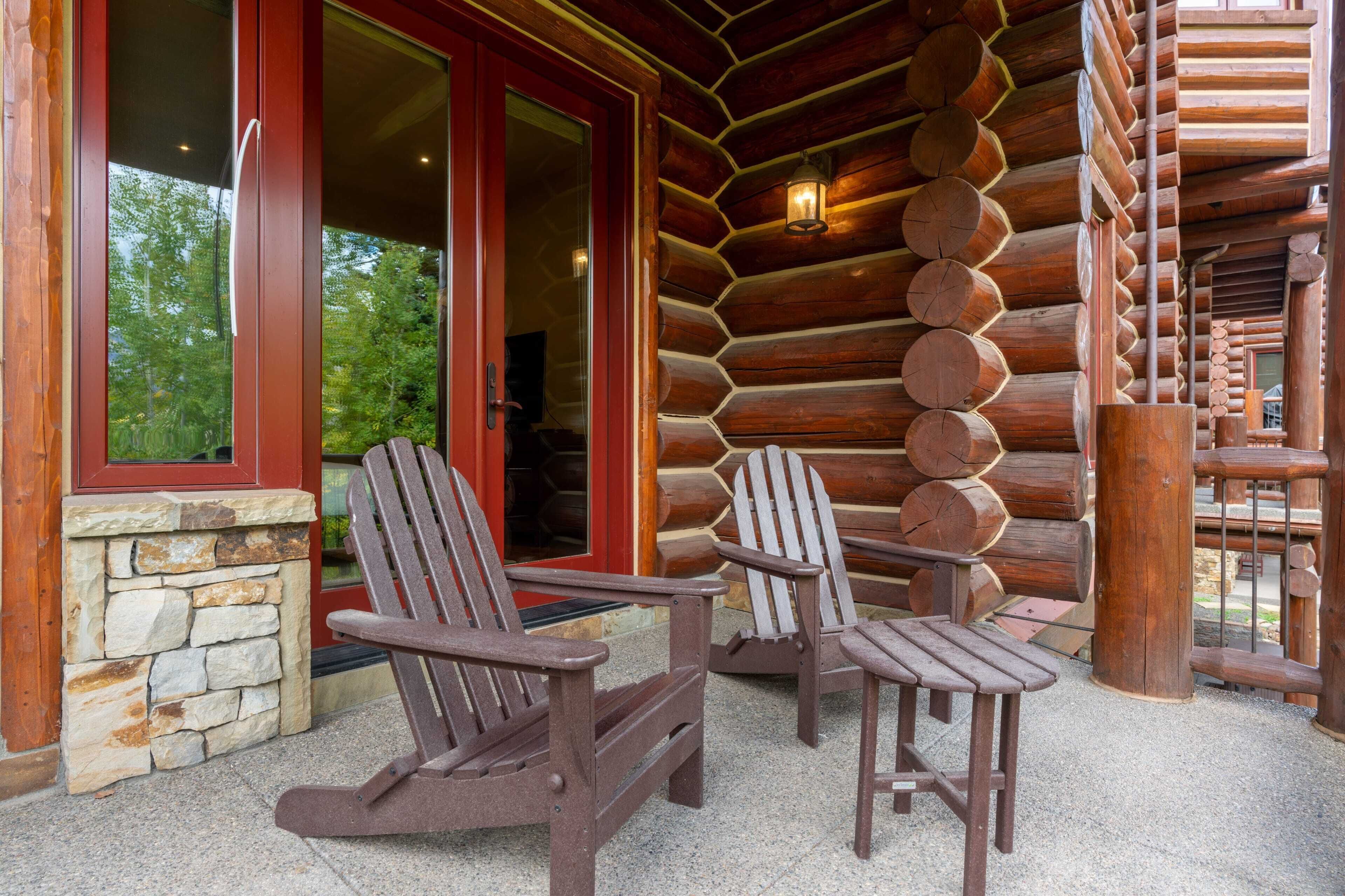 A log cabin with two Adirondack chairs outside, a stone wall, and a wooden staircase.