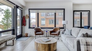 Ett modernt vardagsrum med ett stort fönster, ett runt soffbord, två läderfåtöljer, en soffa och ett litet sidobord med en lampa.