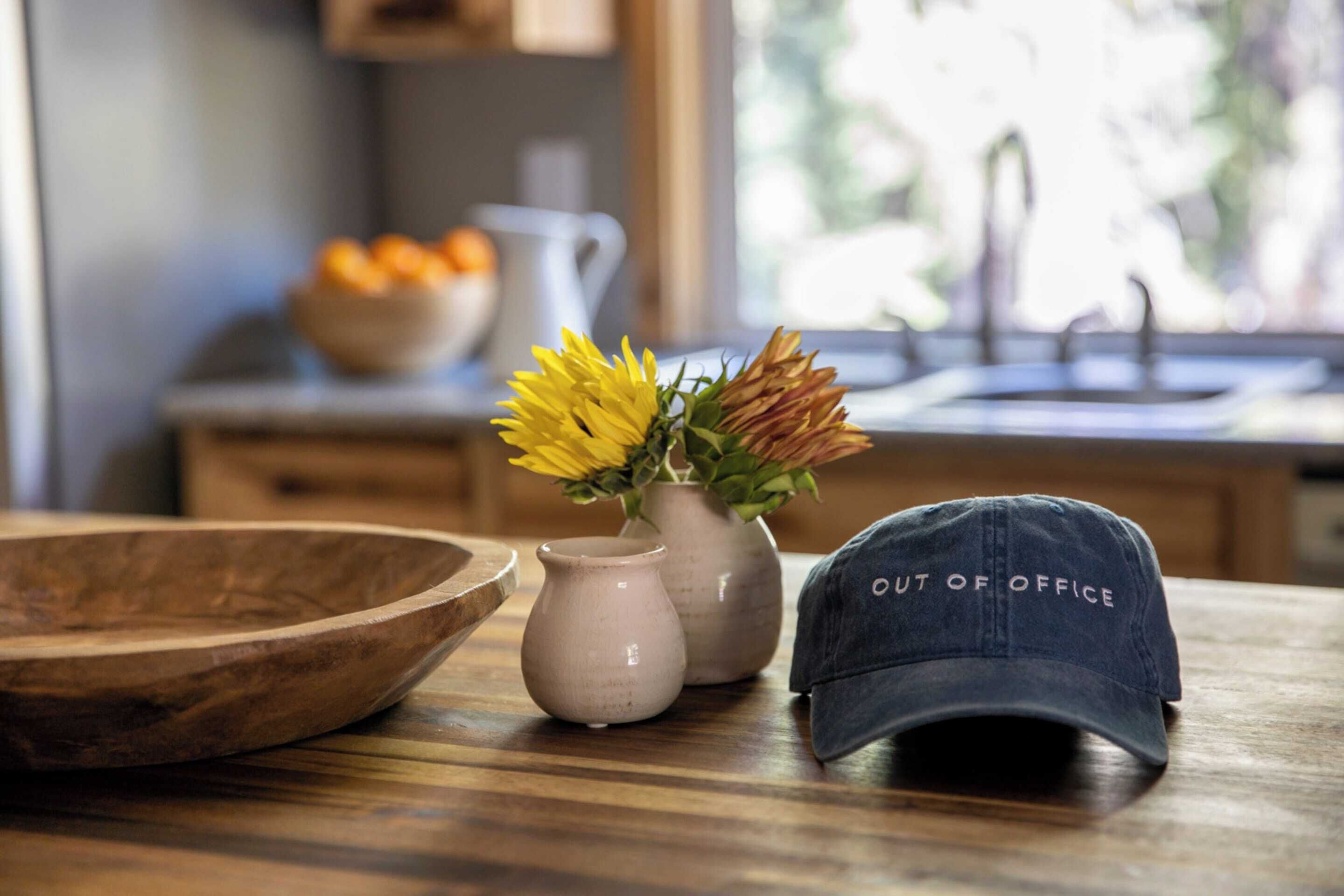 Un bol en bois, deux vases en céramique ornés de fleurs jaunes et une casquette sur laquelle est inscrit « ABSENT », le tout posé sur une table en bois.