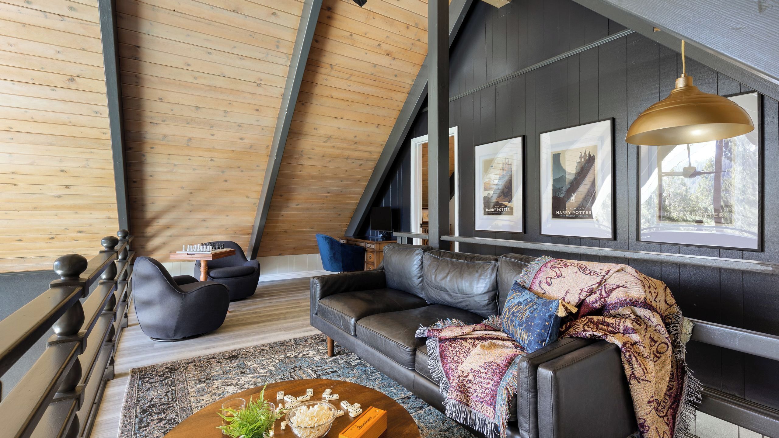 Un salon moderne de style « loft », doté d’un plafond en pente, d’un canapé gris foncé, d’une table basse avec des collations et d’œuvres d’art encadrées accrochées aux murs.