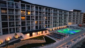 Un hotel a più piani con balconi, una piscina e un giardino curato.