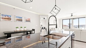 Una cucina moderna con un piano di lavoro in granito, lavello in acciaio inossidabile e zona pranzo con una panca e piante in vaso.
