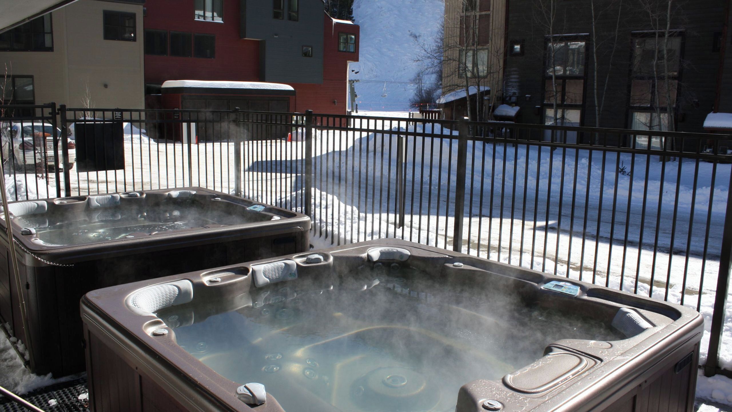 Two hot tubs on a patio with a view of a snowy street and buildings.