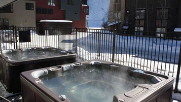 Two hot tubs on a patio with a view of a snowy street and buildings.