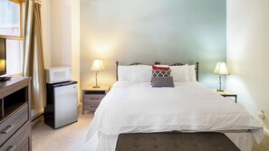 Ein Hotelzimmer mit einem Bett, Nachttischen, einem Schreibtisch mit Mikrowelle, einem kleinen Kühlschrank und einem Fenster mit Vorhängen.