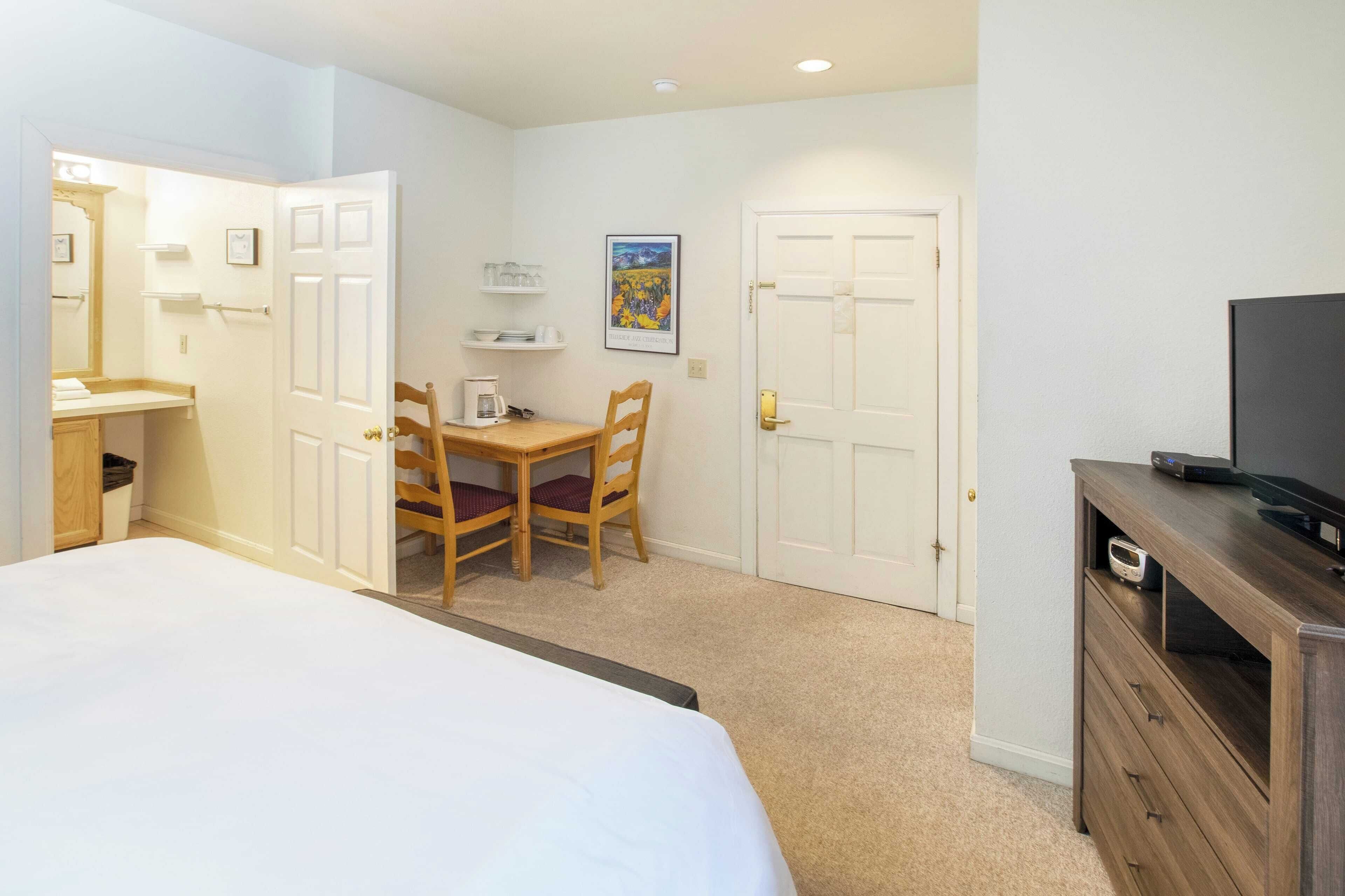 A hotel room with a bed, a desk with a chair, a television on a wooden cabinet, and a door.
