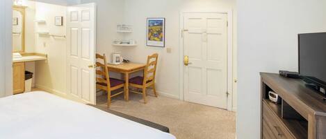 A hotel room with a bed, a desk with a chair, a television on a wooden cabinet, and a door.
