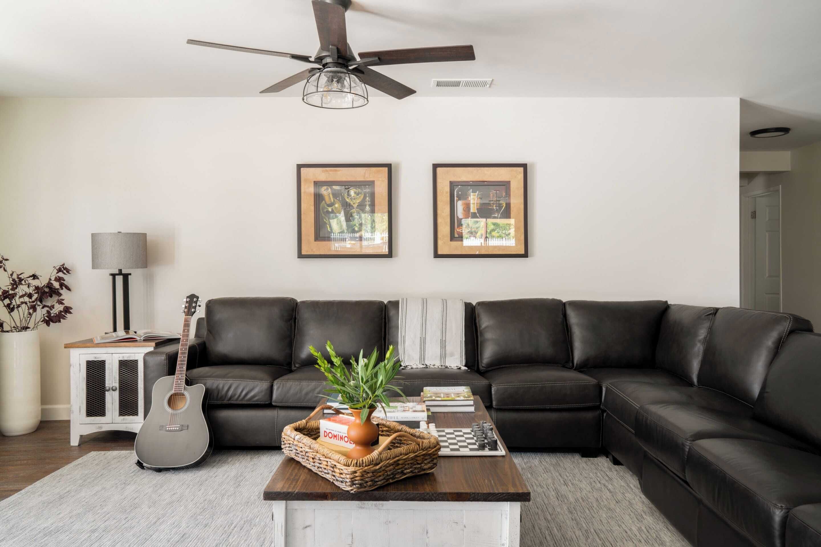 A modern living room with a sectional sofa, a coffee table, a guitar, and framed artwork on the wall.