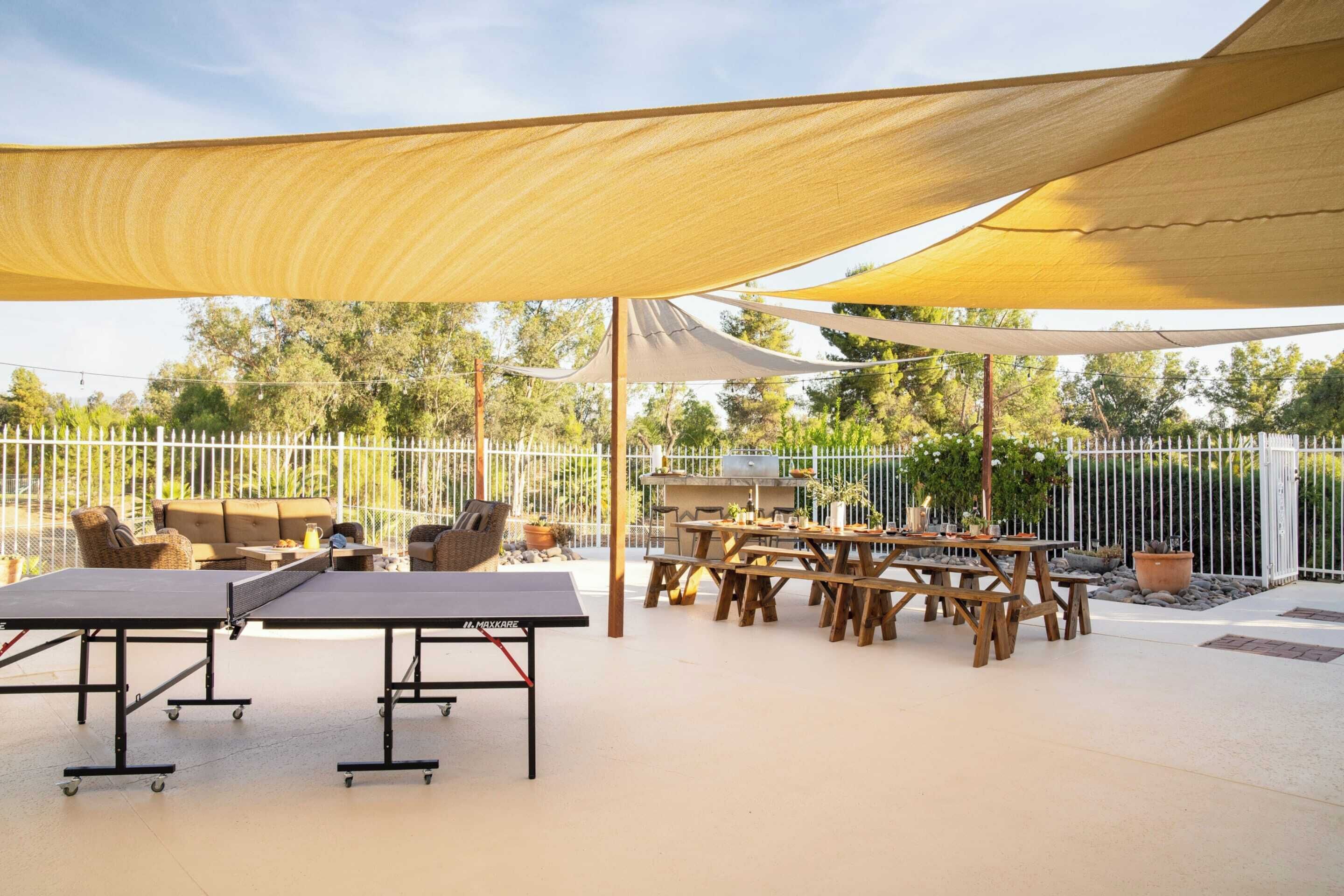 An outdoor patio with ping pong tables, wooden benches, and a grill area.