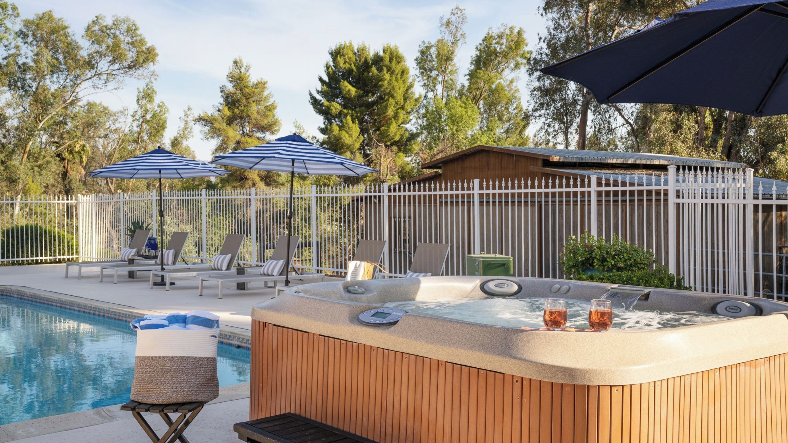 A hot tub with a control panel, lounge chairs, and umbrellas near a pool.