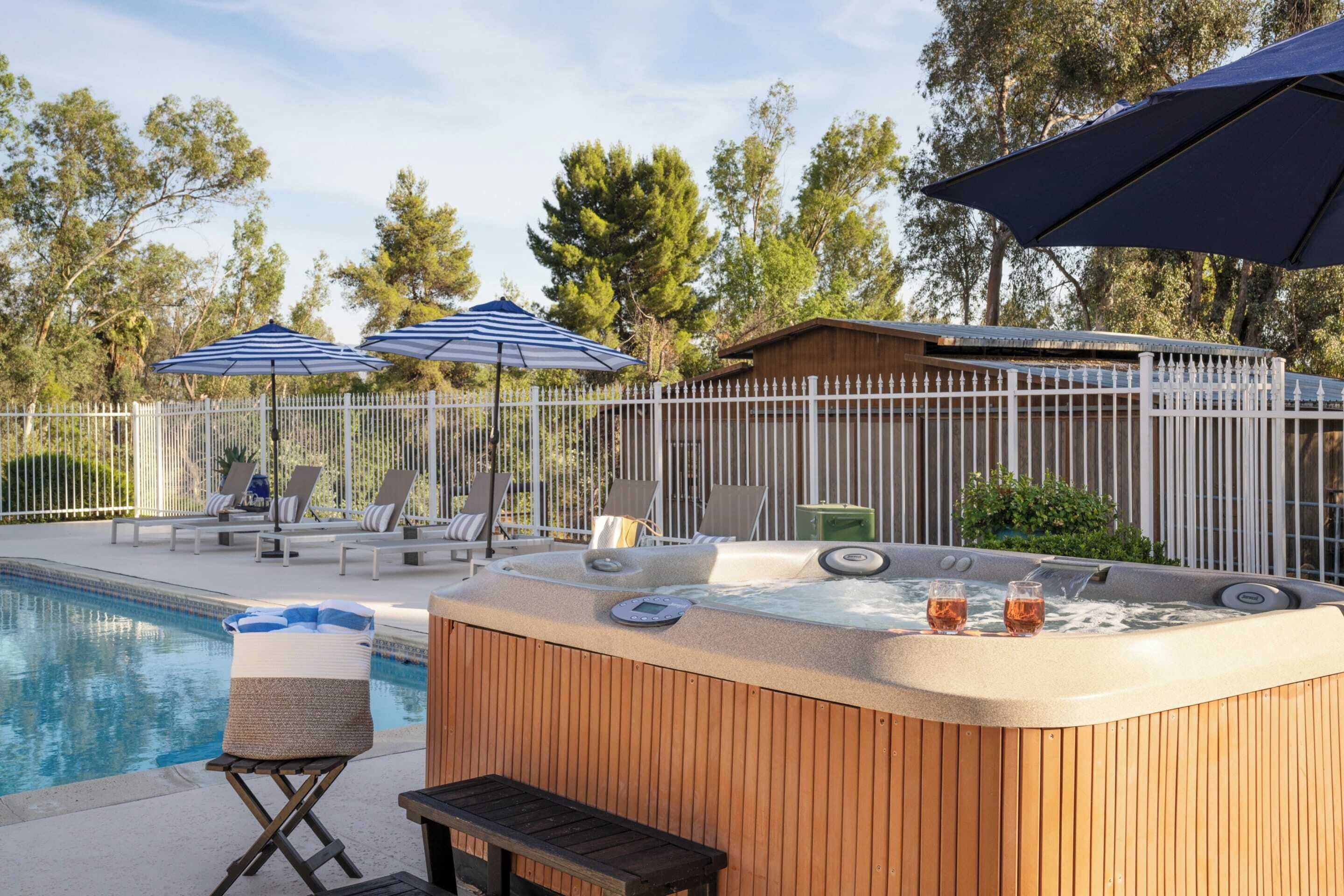 A pool area with lounge chairs, umbrellas, and a hot tub.