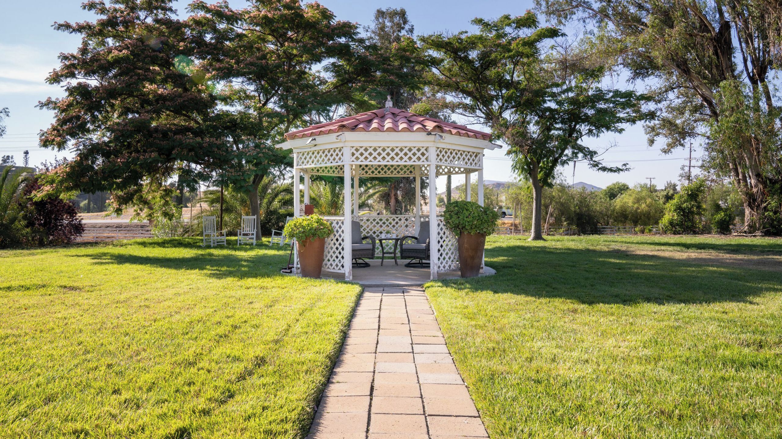 A gazebo with a tiled roof, surrounded by grass and trees.