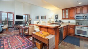 A spacious living area with a large window, a fireplace, and a kitchen with wooden cabinets and stainless steel appliances.